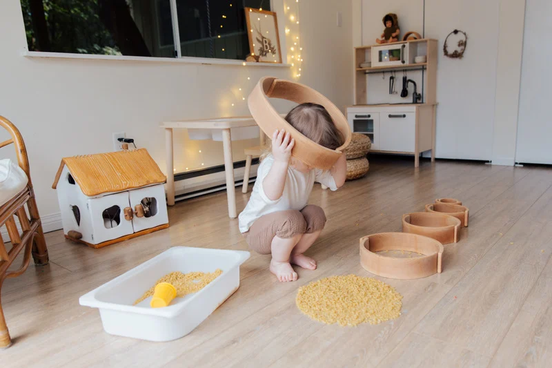 Niño pequeño jugando con aros y pasta en una actividad sensorial de aprendizaje tridimensional.