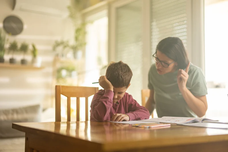 Madre intentando ayudar a su hijo frustrado con los deberes.