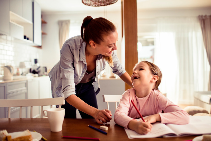 Una niña hace los deberes feliz en la cocina, su madre crea un buen ambiente de estudio