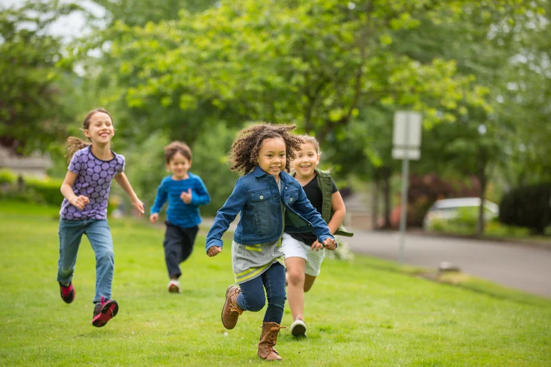 Un grupo de cuatro niños y niños de primaria corre en el parque simbolizando que el tiempo libre forma parte del aprendizaje. Descansar ayuda a no odiar hacer los deberes.
