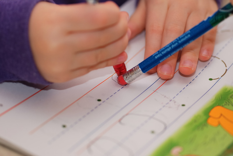 Manos de un adulto corrigiendo con un lápiz la escritura de un niño, mostrando un acompañamiento intrusivo durante los deberes.