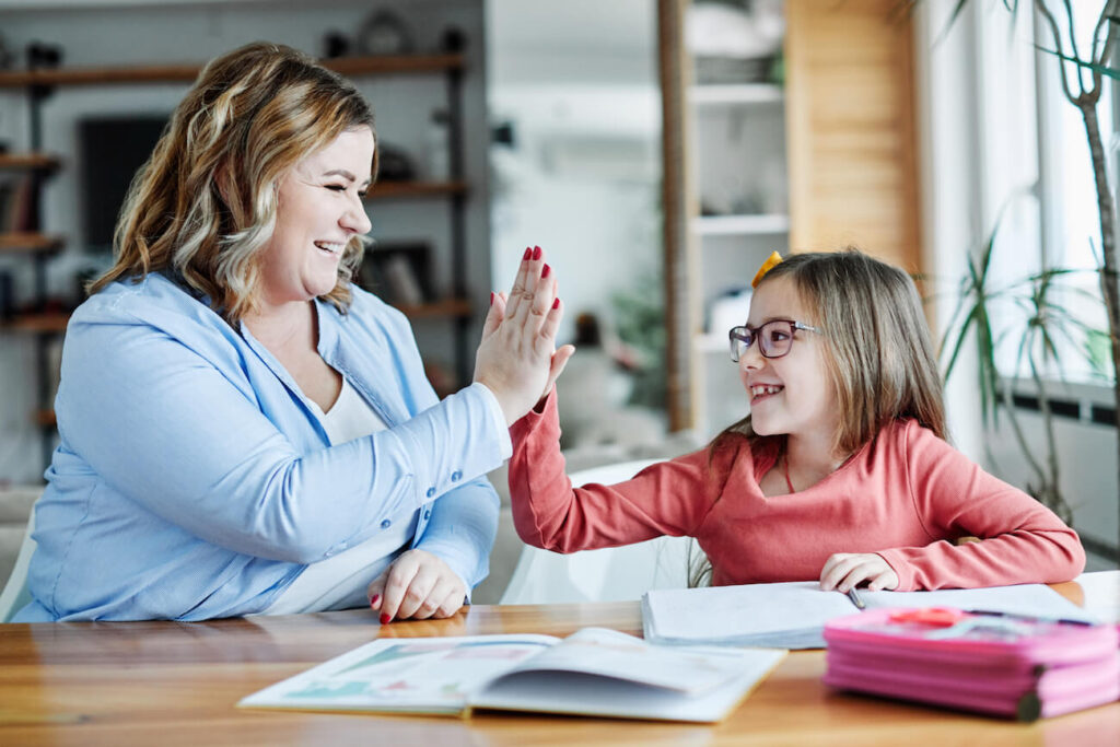 Madre e hija disfrutando juntas del aprendizaje en casa, celebrando un logro con un high-five.