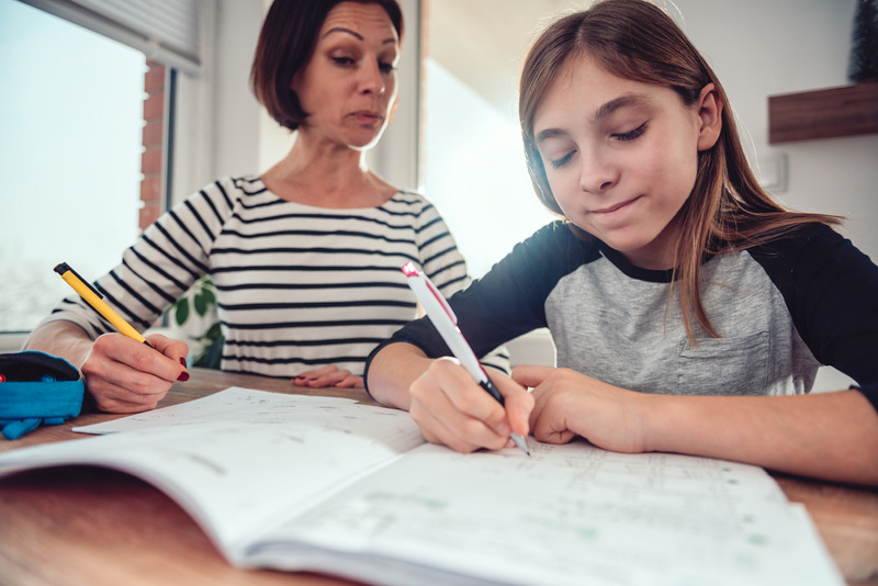 Madre sentada con su hija mientras hace los deberes, mostrando tensión emocional contenida.