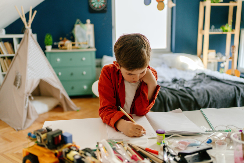 Niño escribiendo en su cuaderno en su habitación, ejemplo de autonomía en los deberes sin intervención de los padres.
